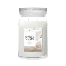 Una candela in un grande barattolo di vetro denominata “Soft Blanket - Giara Grande - Yankee Candle” è realizzata in cera bianca, ha due stoppini e presenta un’etichetta che raffigura una morbida coperta e un orsacchiotto su un letto.