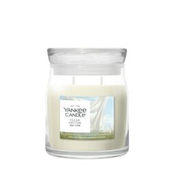 Clean Cotton - Giara Media - Yankee Candle presenta una cera profumata al cotone bianco in un barattolo di vetro con coperchio trasparente, etichettato con lenzuola bianche su uno stendino contro un cielo blu.
