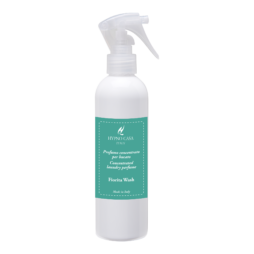 Un flacone spray bianco con l'etichetta "Spray Tessuto - Fiorita Wash - Hypno Casa - 250 ml", caratterizzato da un'etichetta turchese e da un tappo trasparente, è ripreso su uno sfondo semplice. Questo elegante spray per tessuti infonde ai tuoi tessuti l'incantevole profumo di Fiorita Wash ad ogni spruzzo.