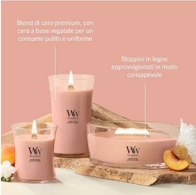 Manuka Nectar – Giara Media – Woodwick Giara media 4 Tre candele WoodWick rosa della linea “Manuka Nectar – Giara Media” sono disposte su una base di legno accanto a fette di pesca. Il testo in italiano ne sottolinea la cera vegetale di alta qualità e gli stoppini in legno provenienti da fonti responsabili. Sia lo sfondo che la superficie sono di colore rosa chiaro.