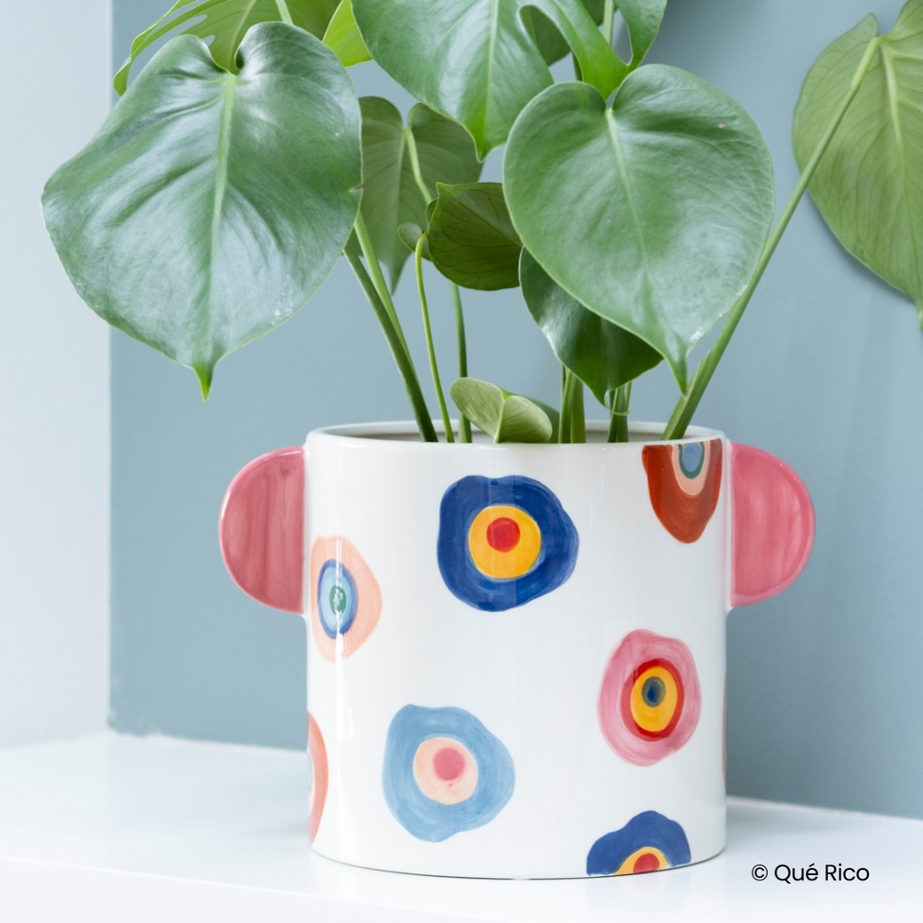 Vaso o Porta Vaso in Ceramica – Valeria – Querico Porta Vasi 2 Nel Vaso in Ceramica - Valeria - Querico, prospera una pianta con grandi foglie verdi. Questo vaso bianco è splendidamente decorato con vivaci motivi circolari in blu, rosso, giallo e bianco e vanta graziosi manici rosa a forma di orecchie su ogni lato.