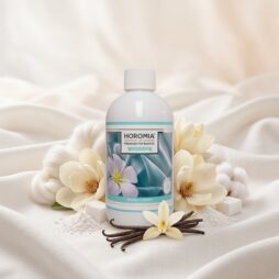 Un flacone da 500 ml di Profuma Bucato - Bianco Infinito di Horomia è esposto con fiori bianchi, bacche di vaniglia e pietre decorative su un tessuto morbido, che riflette la fresca essenza di questa fragranza per tessuti.