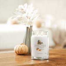 Woodland Weekend Memories – Candela Grande – Yankee Candle Woodland Weekend Memories 2 Ricordi di un fine settimana nel bosco: la Candela Grande di Yankee Candle in un barattolo di vetro è appoggiata su un tavolo di legno, con una zucca beige e fiori bianchi secchi nelle vicinanze, evocando un'accogliente atmosfera autunnale.