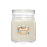 Un barattolo di vetro trasparente di Giara Media contiene una Yankee Candle bianca etichettata "Vanilla Flurries", con immagini di vaniglia, un coperchio rotondo e 368 grammi di cera.