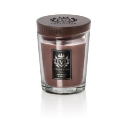 La candela Patchouli & Musk - Candela Media - Vellutier è una candela marrone in un vaso di vetro trasparente con coperchio in legno scuro, caratterizzata da note di patchouli e muschio. Il suo design elegante e la firma del logo spiccano su uno sfondo bianco.