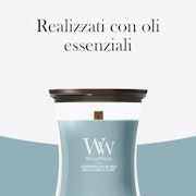 Cedarwood & Ocean Moss – Candela Media – Woodwick Giara media 2 È raffigurata una candela “Cedarwood & Ocean Moss” di Candela Media - Woodwick con coperchio in legno, che evoca i profumi rilassanti del legno di cedro e del muschio marino. Il testo in italiano sopra recita: “Realizzati con oli essenziali”. Lo sfondo presenta tonalità di bianco e azzurro.