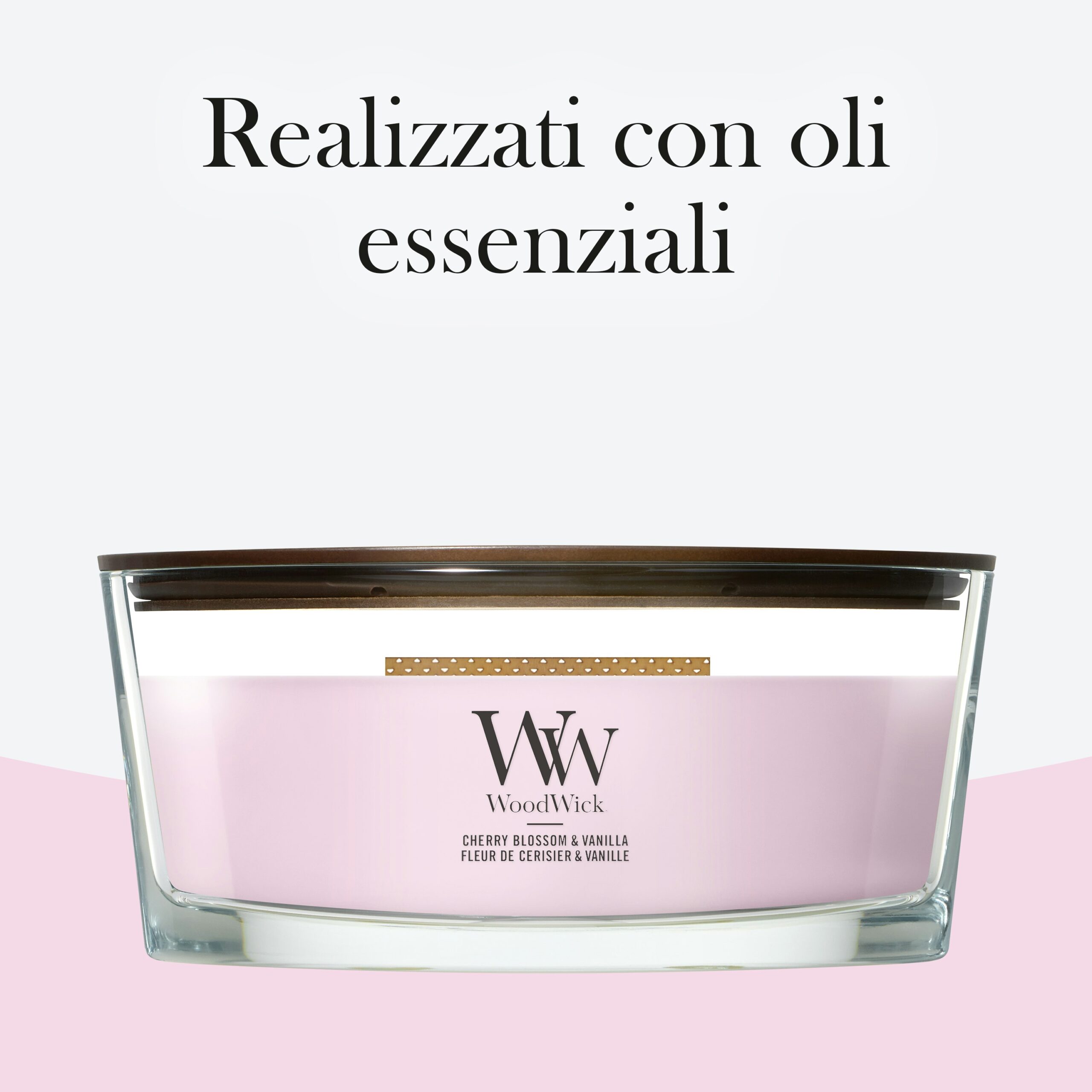 Cherry Blossom And Vanilla – Ellipse – Woodwick Ellipse 4 Una candela WoodWick alla fragranza “Fiori di ciliegio e vaniglia” in un contenitore di vetro rosa con coperchio in legno marrone, delicatamente profumata con note di vaniglia e fiori di ciliegio. La scritta in italiano sopra recita “Realizzati con oli essenziali”.