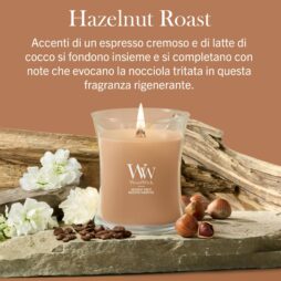 Hazelnut Roast – Candela Media – Wodwick Giara media Una miscela di nocciole tostate - Candela Media - Una candela Wodwick color beige poggia su un pezzo di legno galleggiante accanto a fiori bianchi e nocciole, su uno sfondo marrone con il testo della descrizione della fragranza in italiano.