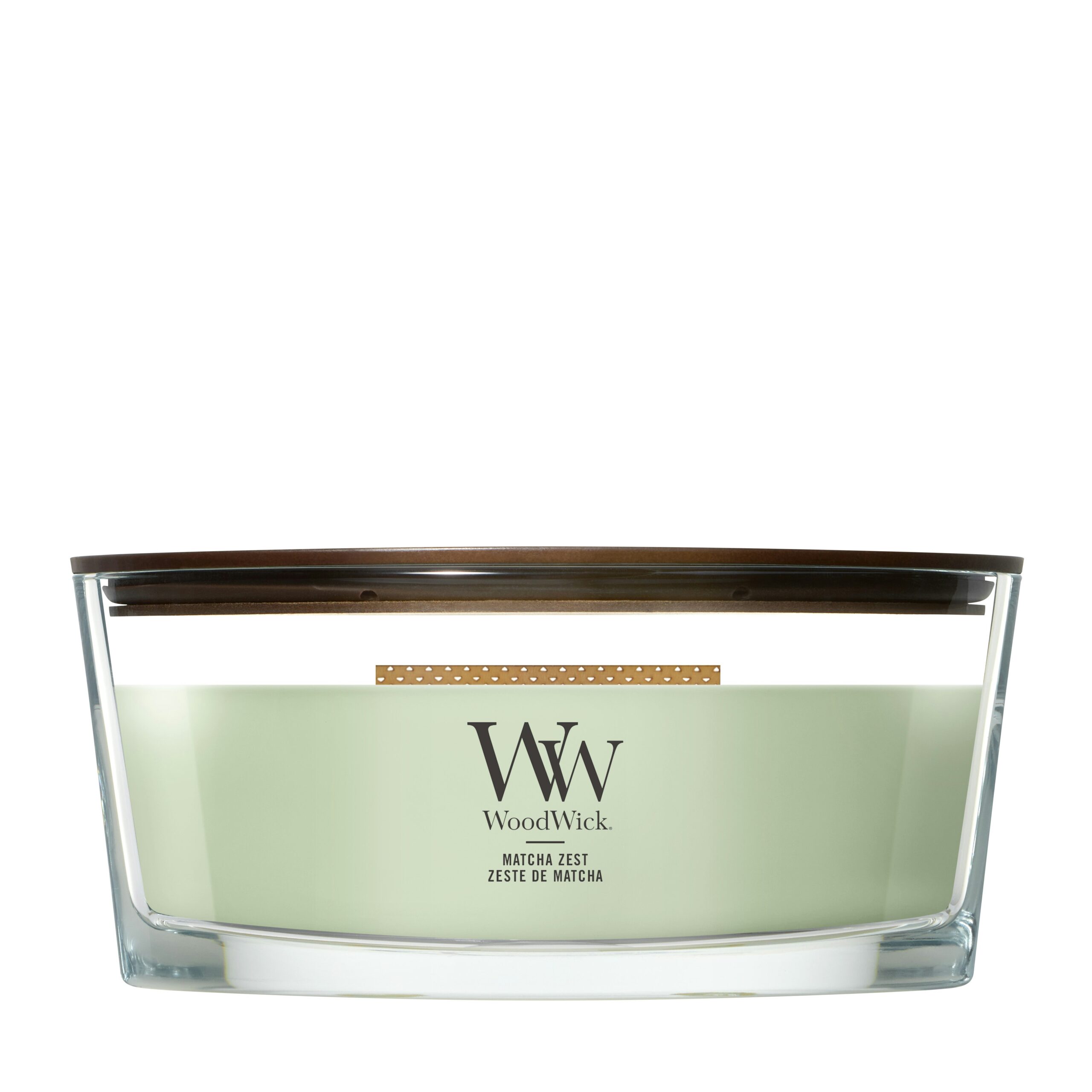 Matcha-Zest – Ellipse – Woodwick Ellipse 4 Una candela Matcha-Zest Ellipse Woodwick è caratterizzata da una cera verde contenuta in un recipiente di vetro di forma ellittica con coperchio in legno. L'etichetta riporta le scritte “WoodWick” e “Matcha-Zest”. Il suo stoppino in legno attraversa la parte superiore, esaltando sia l'aroma fresco che il design moderno.