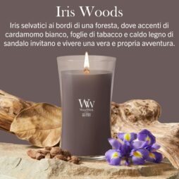 Una candela Iris Woods - Candela Grande - WoodWick è accesa e posizionata su alcune rocce, accanto a pezzi di legno e a un fiore di iris in fiore, il tutto su uno sfondo viola su cui spicca un testo in italiano che ne evidenzia le note olfattive. Questa elegante candela crea un’atmosfera intrisa di raffinatezza e una fragranza perfettamente equilibrata.