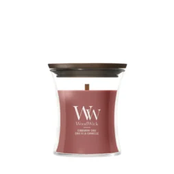 La candela "Cinnamon Chai - Candela Piccola" di WoodWick è una candela rossa contenuta in un barattolo di vetro trasparente a forma di clessidra, dotata di un coperchio in legno e del caratteristico stoppino in legno.