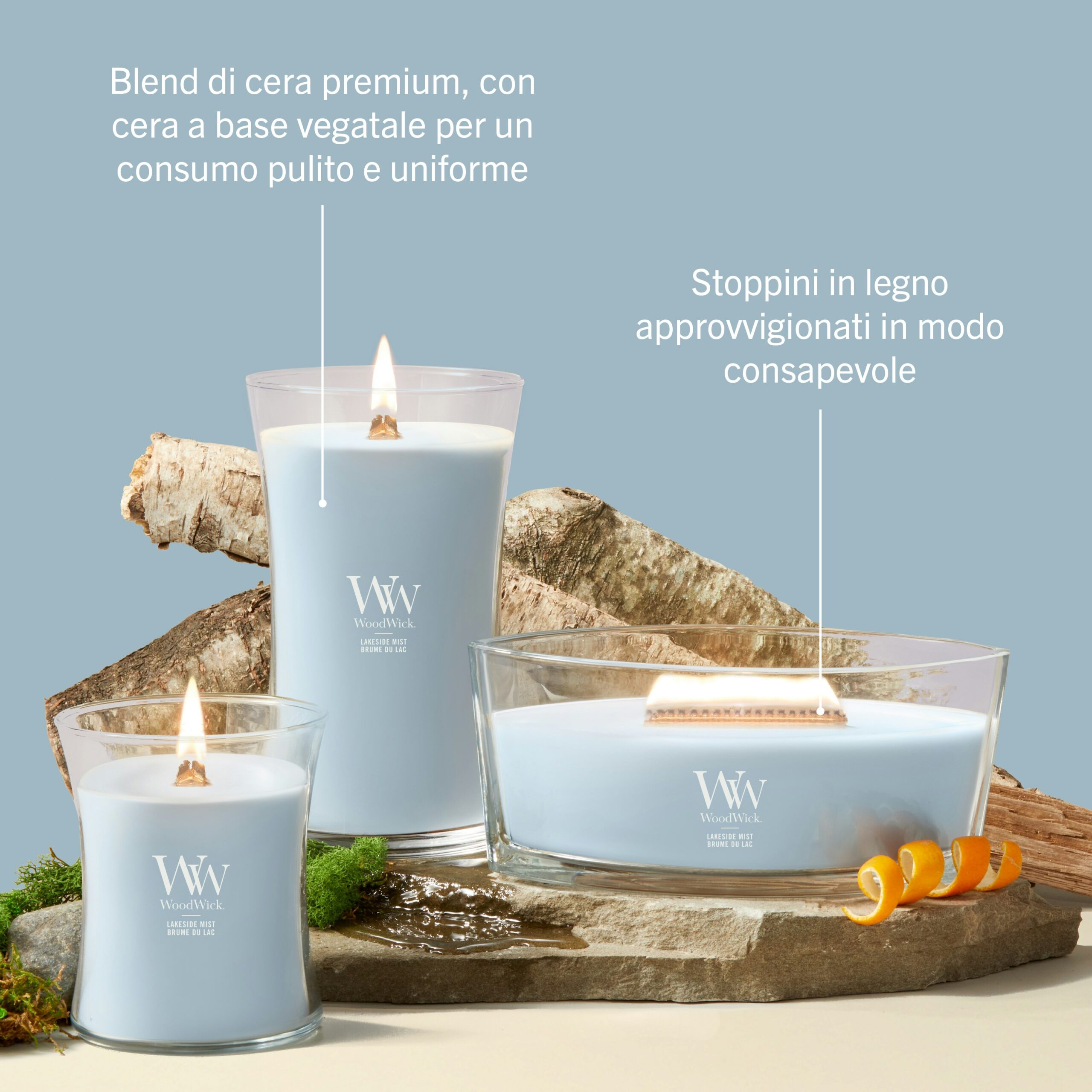 Lakeside Mist – Ellipse – Woodwick Ellipse 5 Tre candele “Lakeside Mist - Ellipse - Woodwick” con cera blu sono disposte su una superficie chiara; una di esse emana una luce soffusa. Bucce d'arancia e rametti verdi impreziosiscono la scena, evocando la fragranza rinfrescante di “Lakeside Mist”. Il testo in italiano descrive la cera di alta qualità e gli stoppini in legno provenienti da fonti responsabili. Lo sfondo è blu.