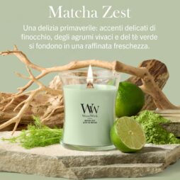 Una candela Matcha-Zest Candela Media - Woodwick di colore verde è accesa e posizionata su una pietra accanto a finocchio, lime fresco, fette di lime e pezzi di legno galleggiante; un testo in italiano su sfondo verde chiaro mette in risalto la fragranza rivitalizzante della candela.