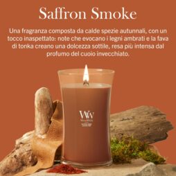A Woodwick Saffron Smoke" - La Candela Grande color marrone arde su una superficie decorata con legno, corteccia e muschio, su uno sfondo marrone a tinta unita con una scritta in italiano che mette in risalto le calde e speziate note di zafferano della candela, mescolate ad aromi dolci.