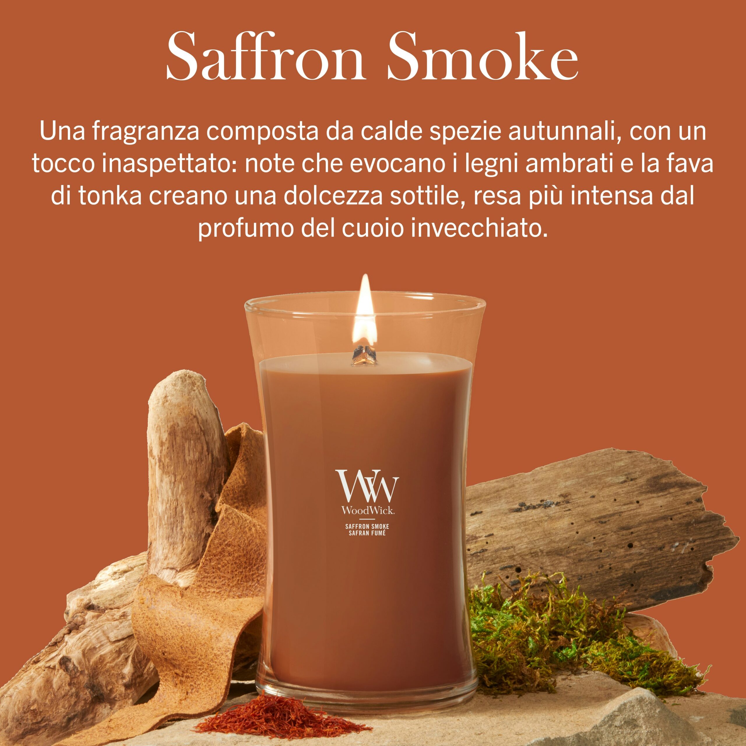 Saffron Smoke – Candela Grande – Woodwick Giara Grande A Woodwick Saffron Smoke" - La Candela Grande color marrone arde su una superficie decorata con legno, corteccia e muschio, su uno sfondo marrone a tinta unita con una scritta in italiano che mette in risalto le calde e speziate note di zafferano della candela, mescolate ad aromi dolci.