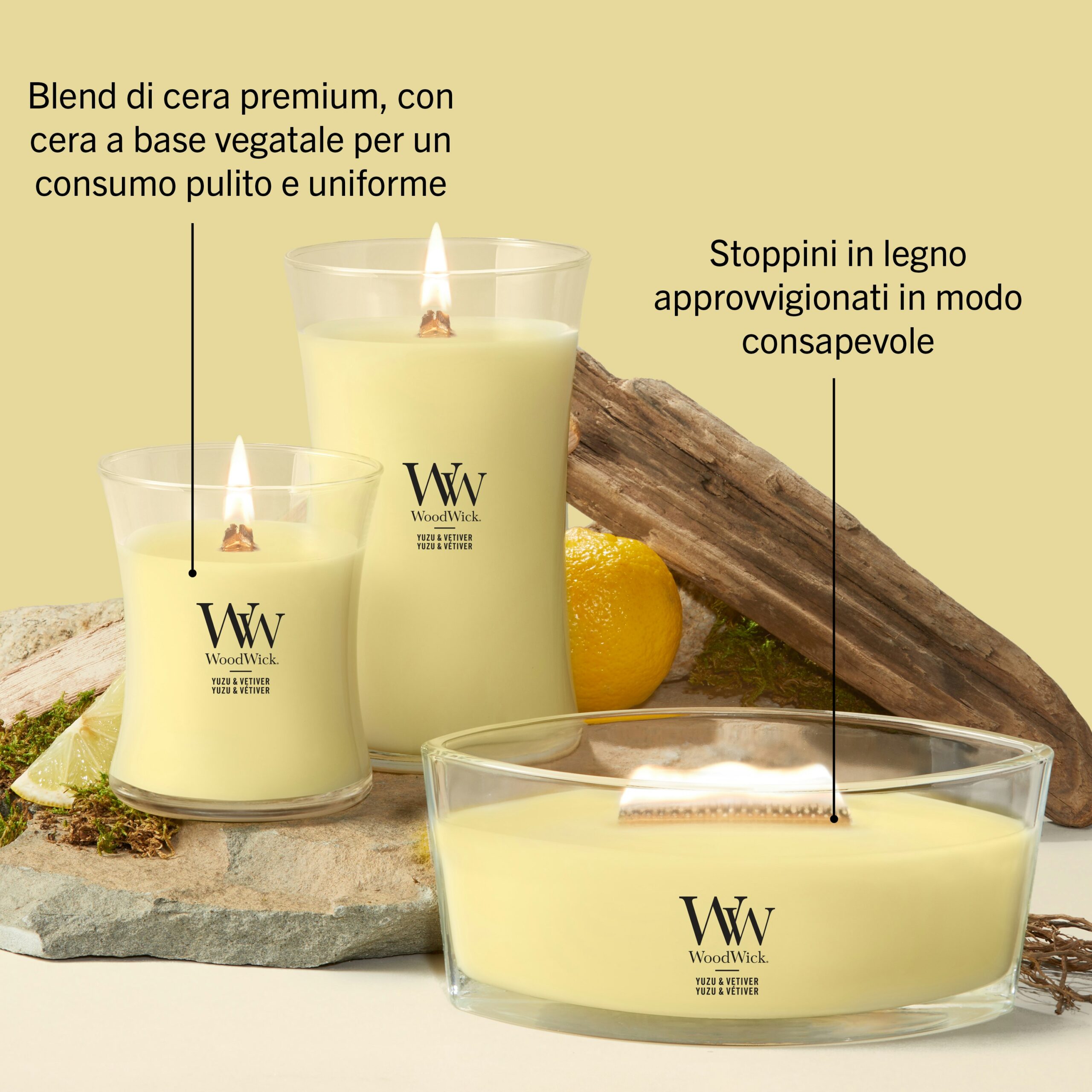 Yuzu & Vetiver – Candela Grande – WoodWick Giara Grande 2 Tre candele gialle WoodWick Yuzu & Vetiver Candela Grande, di diverse dimensioni, poggiano su una superficie in pietra, accompagnate da pezzi di legno e da un limone, evocando la fragranza rinvigorente dello yuzu e del vetiver. Il testo in italiano sottolinea la miscela di cera vegetale di alta qualità e gli stoppini in legno provenienti da fonti responsabili.