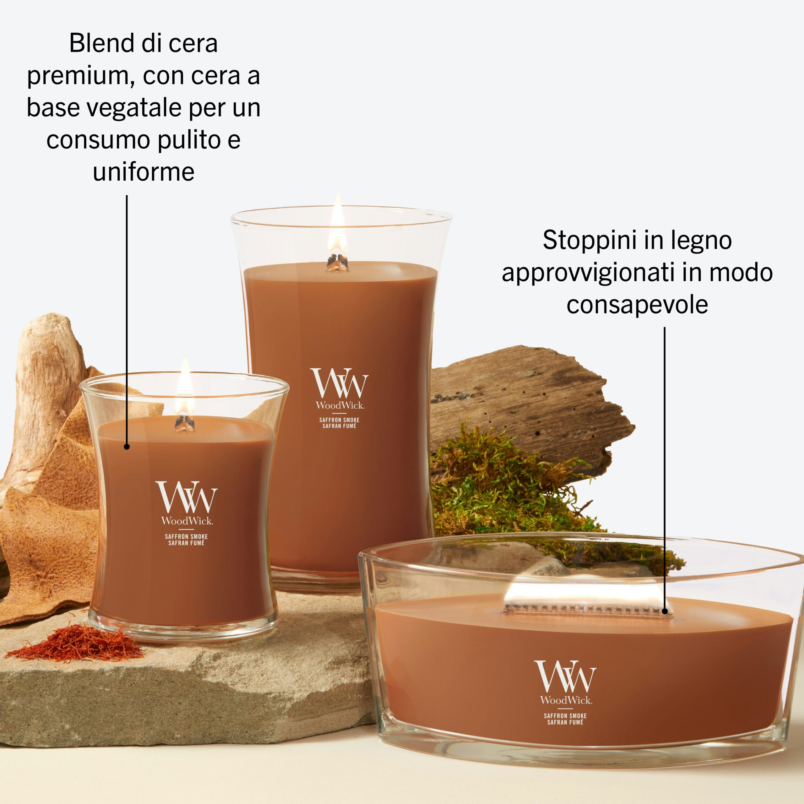 Saffron Smoke – Ellipse – WoodWick Ellipse 4 Tre candele Saffron Smoke - Ellipse - WoodWick in contenitori di vetro marrone sono disposte insieme a muschio e corteccia. Il testo in italiano sottolinea la qualità superiore della cera di origine vegetale, gli stoppini in legno provenienti da fonti responsabili e il delicato aroma di zafferano che si diffonde nell'ambiente.