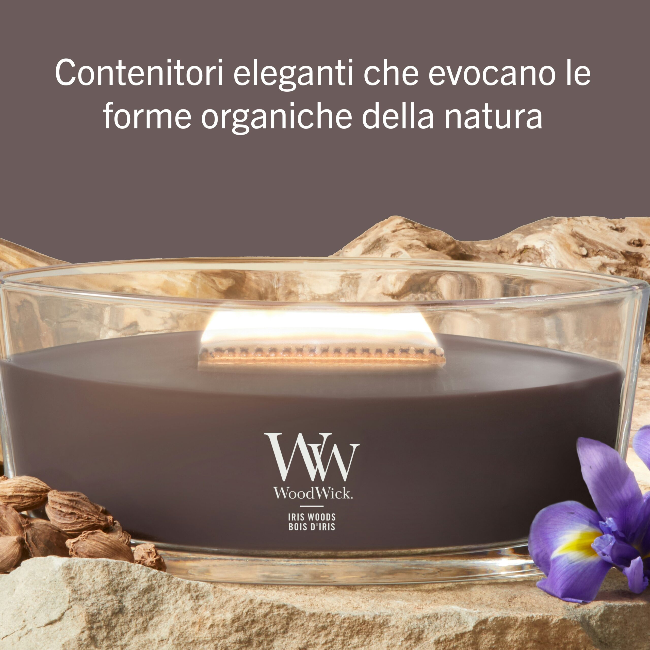 Iris Woods – Ellipse – Woodwick Ellipse 3 Una candela Iris Woods - Ellipse - Woodwick, contenuta in un recipiente di vetro, è adagiata tra elementi naturali quali pietre, noci e un fiore di iris viola. Il testo in italiano riportato sopra fa riferimento a eleganti contenitori ispirati alle forme organiche della natura, che riflettono lo spirito rasserenante della collezione Iris Woods.