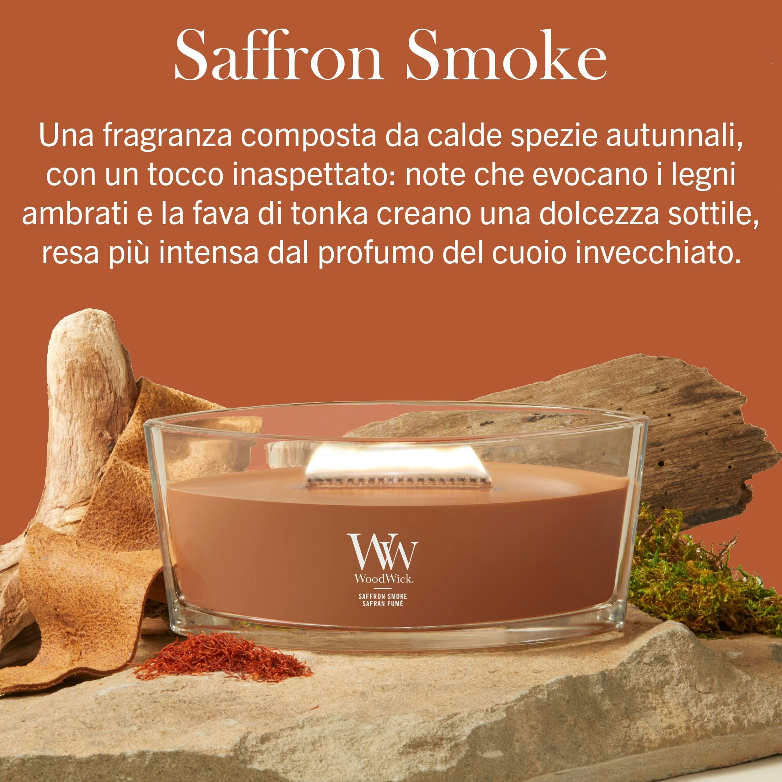 Saffron Smoke – Ellipse – WoodWick Ellipse Una candela WoodWick Saffron Smoke - Ellipse poggia su una superficie di legno, circondata da un ceppo rustico e da erbe autunnali. Sopra, una descrizione in italiano della fragranza crea l’atmosfera, mentre la delicata luce ellittica della candela proietta ombre calde, accentuando le ricche note di zafferano della scena.