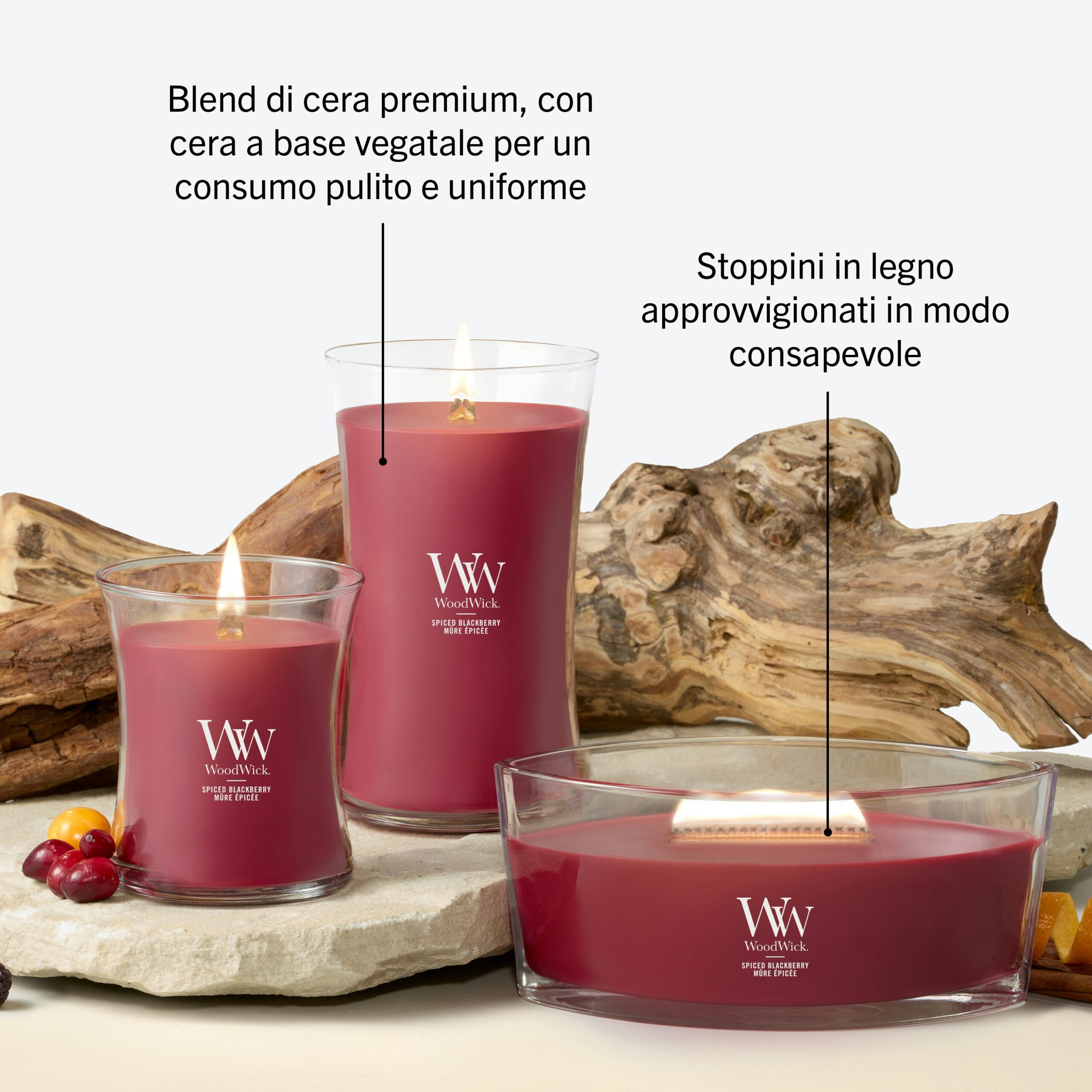 Spiced Blackberry – Candela Grande – Woodwick Giara Grande 5 Tre candele “Spiced Blackberry - Candela Grande - Woodwick” rosse, di diverse forme e dimensioni, sono accese e disposte su una superficie bianca accanto a ceppi di legno e bacche, evocando il ricco aroma di “Spiced Blackberry”. Il testo in italiano sottolinea come caratteristiche principali la miscela di cera di alta qualità e gli stoppini in legno provenienti da fonti responsabili.