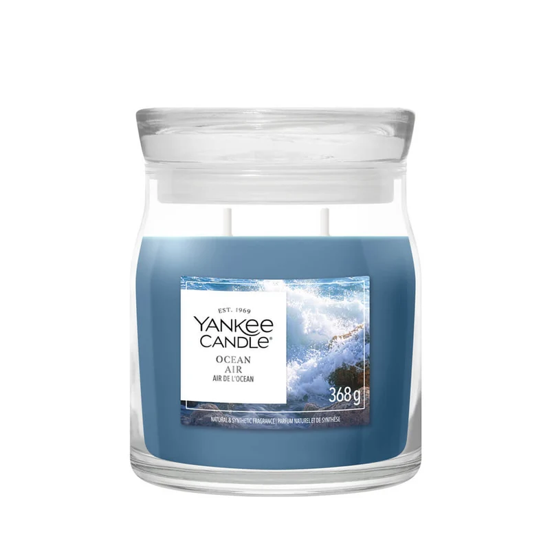 Ocean Air – Candela Media – Yankee Candle 250 Punti Una candela Yankee Candle da 368 grammi con due stoppini, contenuta in un barattolo di vetro con l'etichetta “Ocean Air – Candela Media – Yankee Candle”, che raffigura un'onda dell'oceano.